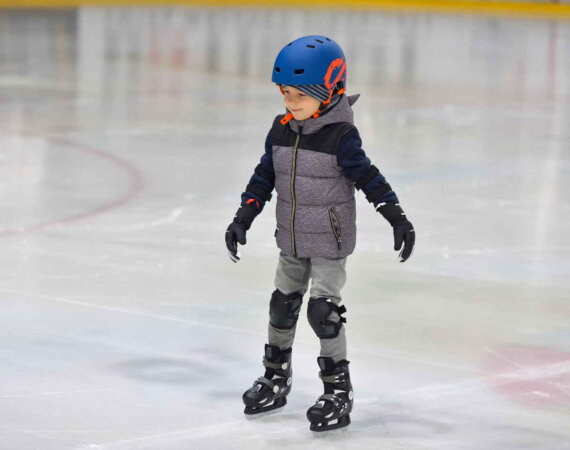 Adorable Little Boy In Winter Clothes With Protections Skating O