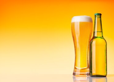 Beer bottle and glass with lager beer in front of yellow background. Studio shot with copy space